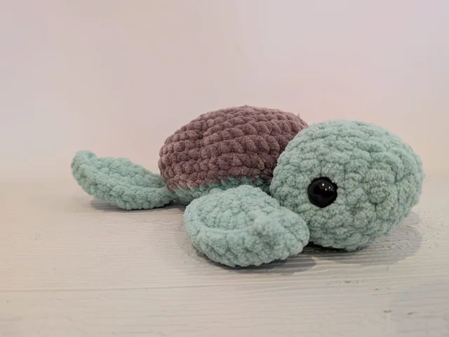 Mint-green crocheted turtle with a brown shell and black eye.